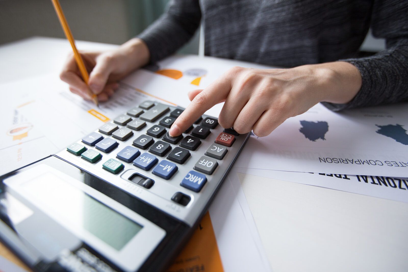 Man tecleando nunha calculadora sobre documentos con gráficos financeiros